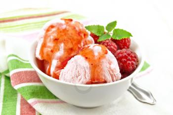 Ice cream crimson with raspberry berries, syrup and mint in white bowl, a spoon on napkin on wooden board background