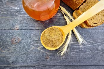 Malt in a spoon, bread, kvass in a glass jug and spikelets on the background of wooden board from above