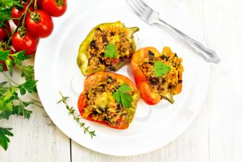 Pepper sweet, stuffed with mushrooms, tomatoes, couscous and cheese in a white plate on a napkin, a fork, parsley against the background of a wooden board from above
