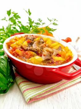 Ragout of turkey meat, tomato, yellow sweet pepper and onion with sauce in a brazier on a towel against the backdrop of a light wooden board