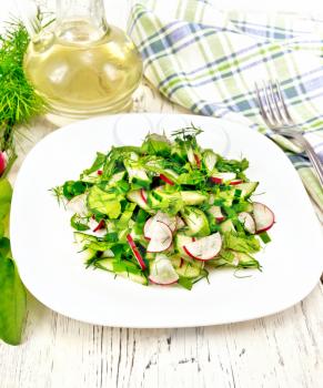 Salad of radish, cucumber, sorrel and greens, dressed with vegetable oil in a plate, napkin on wooden board background