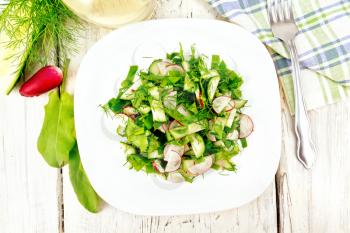 Salad of radish, cucumber, sorrel and greens, dressed with vegetable oil in a plate on a background of light wooden board on top