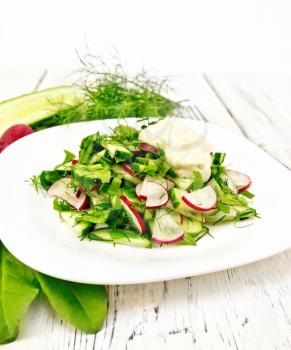 Salad of radish, cucumber, sorrel and greens, dressed with mayonnaise in a plate on the background of light wooden board