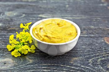 Mustard sauce in a white bowl and flower on a wooden board background