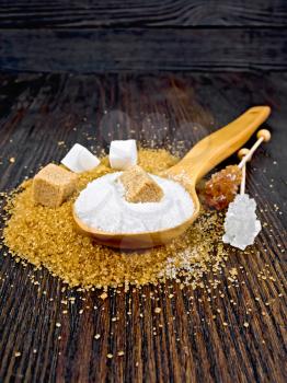 Sugar brown and white in cubes, granulated in a spoon and crystal on a stick against a dark wooden board