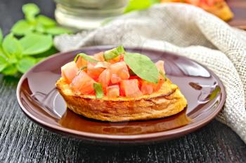 Bruschetta with tomatoes and basil in a plate, napkin and vegetable oil in a decanter against a dark wooden board
