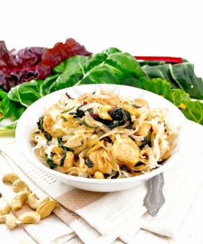 Rice noodles with leafy beet, chicken breast, cashew nuts and soy sauce in a bowl on kitchen towel on wooden plank background