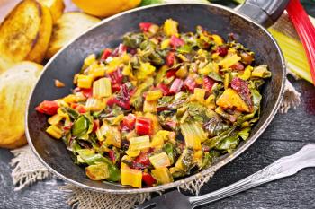 Warm chard salad with orange and onion in a frying pan on sackcloth, bread, fork on a wooden board background