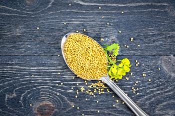 Mustard seeds in a metal spoon with a flower on a wooden board background from above