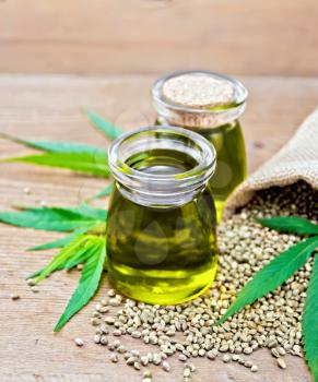 Hemp oil in two glass jars with grain in the bag and on the table, cannabis leaves on the background of an old wooden board