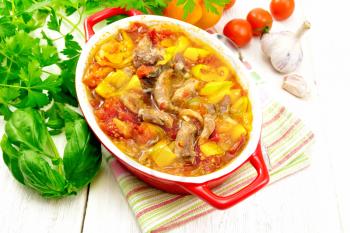 Ragout of turkey meat, tomato, yellow sweet pepper and onion with sauce in a brazier on a napkin on a wooden board background