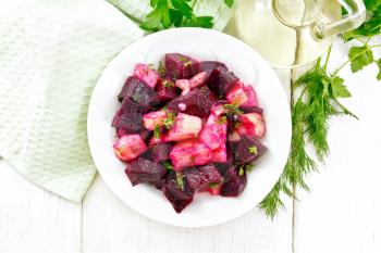 Beetroot and potato salad, seasoned with vegetable oil and vinegar in a plate, napkin, parsley and dill on a wooden board background from above