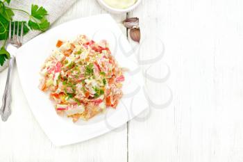 Salad of crab sticks, cheese, garlic and tomatoes, dressed with mayonnaise, napkin and parsley on a wooden board background from above