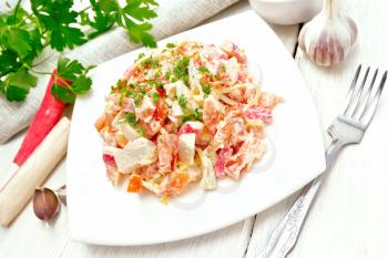 Salad of crab sticks, cheese, garlic and tomatoes, dressed with mayonnaise, towel and parsley on a wooden board background