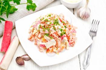Salad of crab sticks, cheese, garlic and tomatoes, dressed with mayonnaise, napkin and parsley on the background of a light wooden board