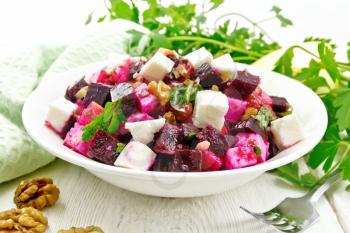 Salad with beetroot, feta cheese, apple, walnuts, parsley, seasoned with balsamic vinegar and olive oil in a plate, a towel against the background of a light wooden board