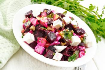 Salad with beets, salted feta cheese, apples, walnuts, parsley, seasoned with balsamic vinegar and olive oil in a plate, green napkin on a wooden board background