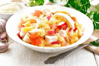 Salad of crab sticks, cheese, garlic, tomatoes and eggs with mayonnaise in a plate, towel, parsley and fork on the background of light wooden boards