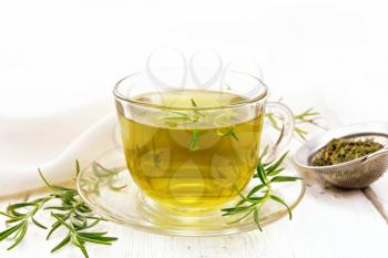 Rosemary herbal tea in a cup, a strainer with dry herb and linen napkin on a wooden board background