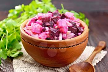 Vinaigrette salad with pickled or sauerkraut, potatoes, beetroot and onions, seasoned with vegetable oil in a bowl on burlap, parsley on a dark wooden board background