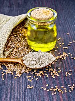 Flax flour in a spoon, oil in a glass jar, linen seeds in a bag on a wooden board background