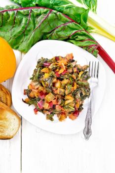 Warm chard salad with orange and onion in a plate, bread, fork on a light wooden board background from above
