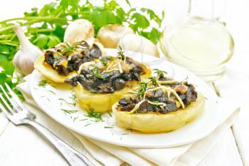 Potatoes stuffed with mushrooms, fried onions and cheese in a dish on kitchen towel, vegetable oil in decanter, parsley, garlic and a fork on wooden board background