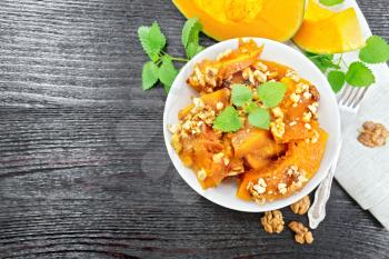 Pumpkin with walnuts and honey in a bowl, napkin and mint on a wooden board background from above