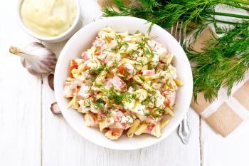 Salad of crab sticks, cheese, garlic, eggs and tomatoes, dressed with mayonnaise in a plate, kitchen towel and parsley on the background of a light wooden board on top