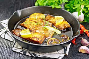 Pink salmon with a sauce of honey, lemon juice, garlic, hot pepper and soy sauce, lemon slices and a sprig of thyme in a frying pan on a towel, parsley on dark wooden background