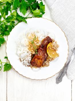 Pink salmon with honey, lemon juice, garlic, hot pepper and soy sauce, boiled rice, slice of lemon and sprig of thyme in a plate, parsley, towel and fork on the background of light wooden board on top