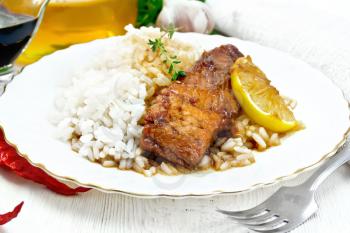Pink salmon with honey, lemon juice and soy sauce, boiled rice, slice of lemon and sprig of thyme in a plate, hot pepper, garlic, parsley, napkin and fork on light wooden board background
