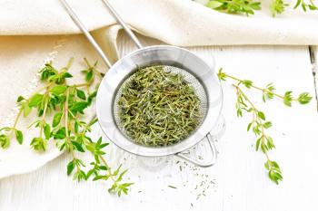 Thyme dry in a metal strainer, fresh greens of grass and linen napkin on a wooden board background
