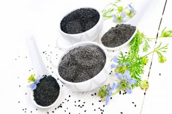 Flour and seeds of black caraway in bowls, sprigs of kalingini with blue flowers and leaves on a background of light wooden board