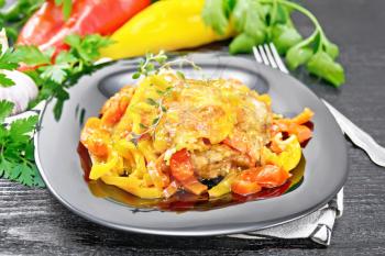Chicken stewed with tomatoes, yellow and red bell peppers and cheese in a plate on towel, thyme, parsley and garlic on black wooden board background