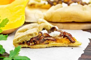 Piece pie of pumpkin, fried onions and soft cheese on parchment, parsley on a wooden board background