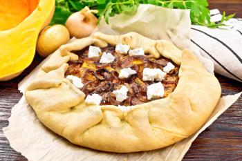 Pie of pumpkin, fried onions and soft cheese on parchment, napkin, parsley on a wooden board background