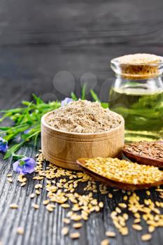 Flaxseed flour in a bowl, white and brown seeds in spoons and on table, flax leaves and flowers, oil in a glass jar on wooden board background