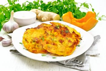 Pumpkin fritters in a plate on napkin, sour cream in a bowl, parsley, garlic and ginger on white wooden board background