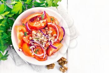 Fresh tomato salad with walnuts and red onions, seasoned with olive oil, vinegar, fenugreek and salt in a plate on a towel on a wooden board background from above
