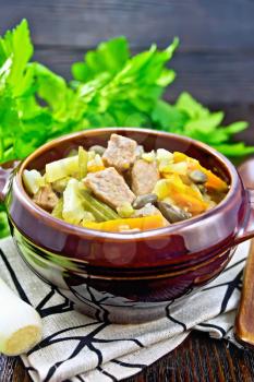 Eintopf soup of pork, celery, beans, carrots and potatoes with leek in a clay bowl on dark wooden board