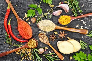 Hot pepper, ginger, fenugreek, turmeric in spoons, nutmeg, cardamom, star anise and coriander, rosemary, parsley, thyme, garlic and chili pods on black wooden board top