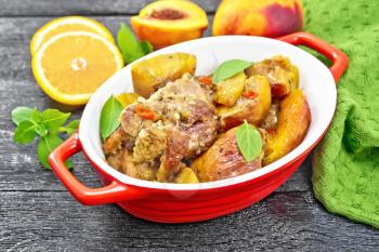 Turkey stewed with peaches, fresh hot pepper and orange sauce, basil leaves in a roasting pan, napkin, fruits on wooden board background