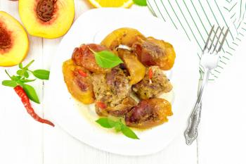 Turkey stewed with peaches, fresh hot pepper and orange sauce, basil leaves in a plate, napkin, fruits on wooden board background from above