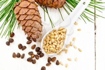 Peeled kernels of cedar nuts in a spoon, two pinecones and nuts in the shell against a light wooden board on top
