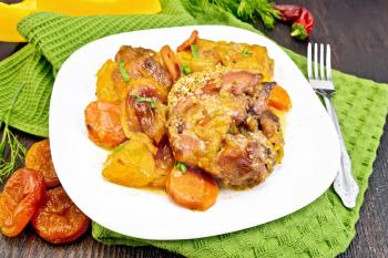 Chicken stew with pumpkin, dried apricots, carrots and red wine, sprinkled with sesame seeds in a plate on green kitchen towel against dark wooden board