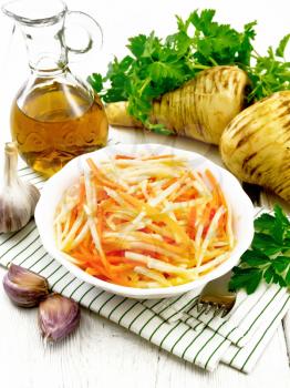 Salad of fresh carrots, parsnip and garlic with vegetable oil in a plate on a towel, fork, parsley and root vegetables on wooden board background