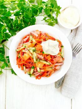 Salad from smoked sausage, spicy carrot, tomato, cucumber and spices with mayonnaise, napkin, fork and parsley on a wooden board background from above
