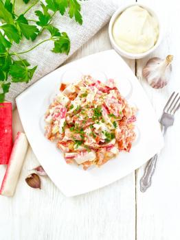 Salad of crab sticks, cheese, garlic and tomatoes, dressed with mayonnaise, towel and parsley on a wooden board background from above