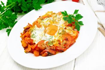 Fried eggs with tomatoes, sweet pepper, onions and herbs in a plate, napkin, parsley and fork on wooden board background